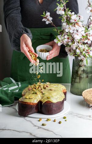 Colomba di Pasqua nelle mani della donna shef, tradizionale torta di colomba pasquale italiana con glassa di pistacchio verde, fiori freschi di primavera, torta di pasqua Foto Stock