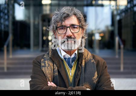 Serio uomo d'affari caucasico di mezza età che guarda la macchina fotografica. Capelli grigi 50 anni in un ambiente di lavoro aziendale. Foto Stock