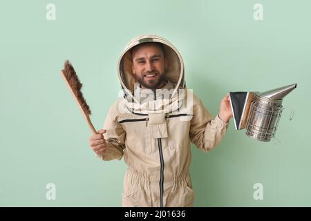 Apicoltore maschio in tuta protettiva con forniture su sfondo verde Foto Stock