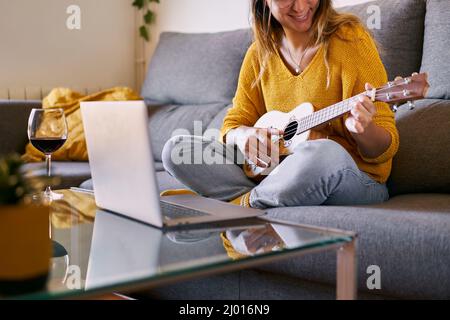 Donna sorridente imparando a giocare online ukulele dal suo laptop. Foto Stock