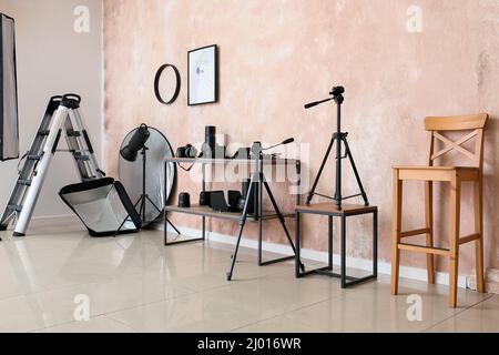 Scaffalatura con attrezzatura di illuminazione e sedia vicino parete rosa in studio fotografico Foto Stock