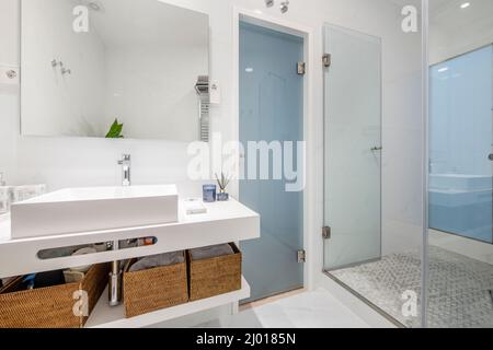 bagno con finiture in porcellana bianca, pareti in piastrelle bianche e pavimenti in marmo, scaldasalviette in acciaio inox e box doccia con divisorio in vetro Foto Stock