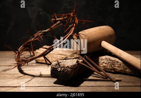 Corona di spine con croce di legno, mazzuolo e unghie su tavola Foto Stock