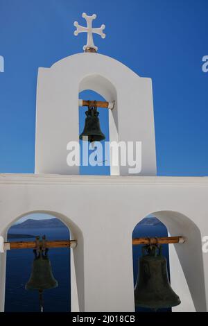 Tre campane della chiesa e una croce religiosa in cima accanto ad una chiesa e una bella vista sul mare egeo a Santorini Foto Stock