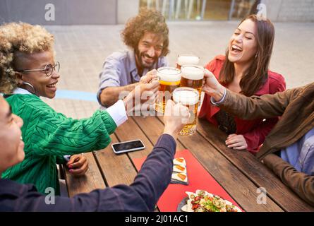 Gruppo di amici felici che tostano con la birra mentre pranzano all'aperto. L'attenzione è rivolta alle birre Foto Stock