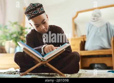 I bambini più che mai hanno bisogno di opportunità. Scatto di un giovane ragazzo musulmano che legge nel salotto di casa. Foto Stock