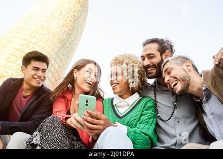 Sorridente gruppo misto di amici che usano il cellulare all'aperto. Amici che si divertono Foto Stock