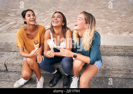 Tre giovani donne che mangiano i coni del gelato e ridono il buon giorno caldo di estate durante la loro vacanza. Gente felice sorridente Foto Stock