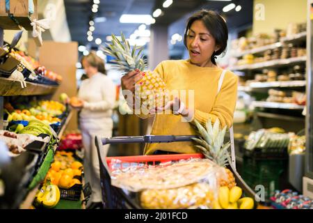 Donna che raccoglie ananas maturo al supermercato Foto Stock