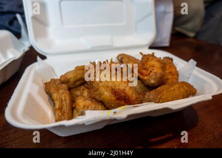 Primo piano, focalizzazione selettiva su un ordine di ali di pollo croccanti in un contenitore bianco in polistirolo da andare su un tavolo da cucina Foto Stock