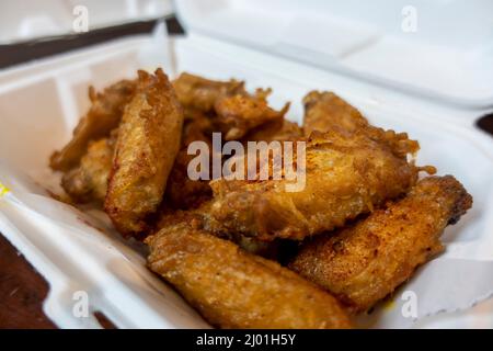 Primo piano, focalizzazione selettiva su un ordine di ali di pollo croccanti in un contenitore bianco in polistirolo da andare su un tavolo da cucina Foto Stock