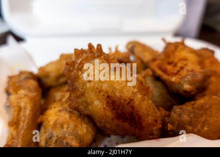 Primo piano, focalizzazione selettiva su un ordine di ali di pollo croccanti in un contenitore bianco in polistirolo da andare su un tavolo da cucina Foto Stock