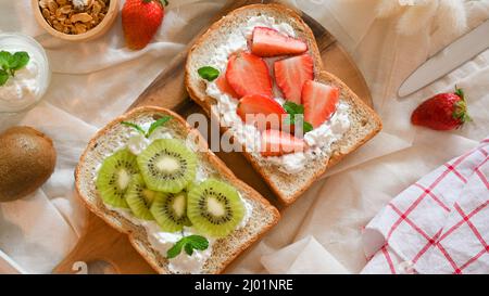 Toast di fragole e kiwi con formaggio fresco fatto in casa su tavola di legno. Colazione sana e dietetica. Foto Stock