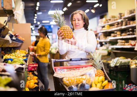 Donna anziana soddisfatta che raccoglie ananas maturo al supermercato Foto Stock