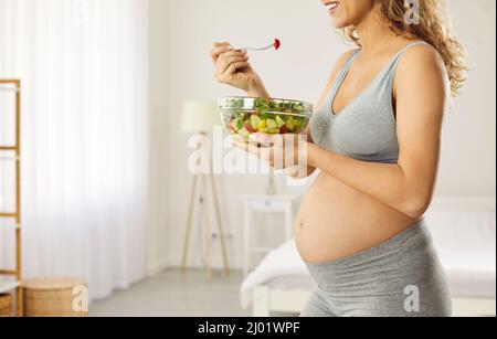 La madre incinta felice che sta attendendo il bambino si prende cura della sua salute e mangia le verdure Foto Stock