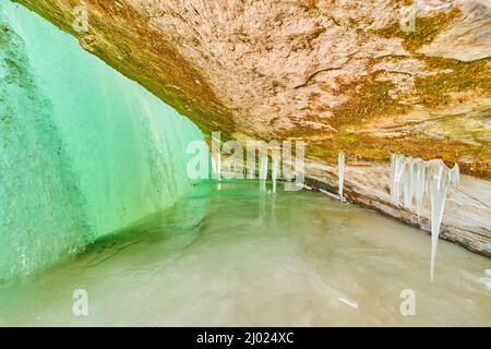Caverna di ghiaccio sul lago ghiacciato con ingresso coperto da cascata verde ghiacciata Foto Stock