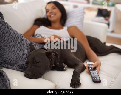 Passare la giornata con il mio ragazzo. Scatto di una giovane donna attraente che si rilassa sul divano con il suo cane. Foto Stock