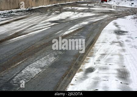 Percorsi da ruote auto, passando auto su una strada invernale nevosa e sciogliente, uno sfondo interessante. Foto Stock