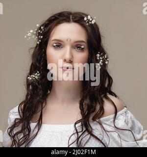 Ritratto giovane bella donna con fiori bianchi su occhi e capelli. Primavera moda foto e cura della pelle ciglia. Foto Stock