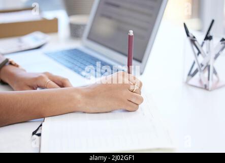 Diarizing eventi importanti. Scatto corto di una donna d'affari irriconoscibile che scrive nel suo notebook mentre lavora alla sua scrivania in ufficio. Foto Stock