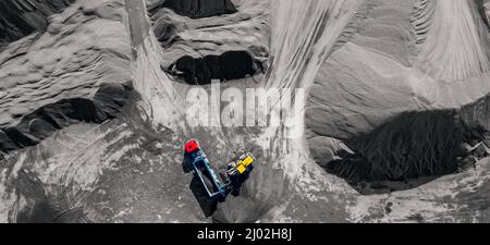 Escavatore industriale a bandiera che carica pietra, pietra frantumata o sabbia nel camion. Vista dall'alto dell'antenna. Foto Stock