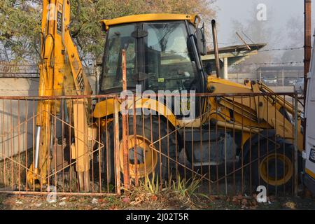 Attrezzatura per l'agricoltura, attrezzatura per la raccolta nei campi. Un grande e potente trattore giallo in piedi dietro una recinzione metallica in un parcheggio. Foto Stock