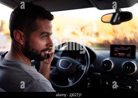bel ragazzo bearded che parla sul telefono cellulare mentre aspetta seduto all'interno della sua auto, tempo libero e tecnologia di comunicazione concetto Foto Stock
