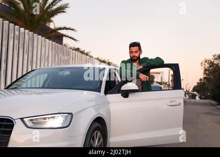 attraente giovane barbuto uomo in piedi accanto alla porta aperta della sua auto in attesa, il tempo libero e concetto di guida, copia spazio per il testo Foto Stock