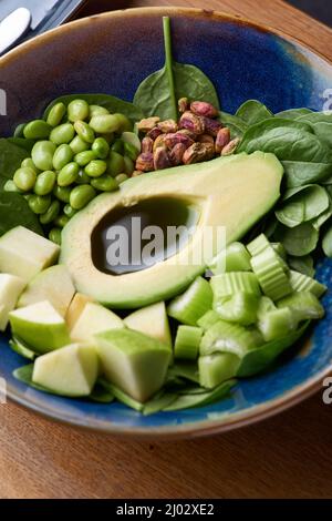 ciotola verde di cibo sano, ciotola vegana con avocado, mela e verdure verdi su sfondo di legno Foto Stock