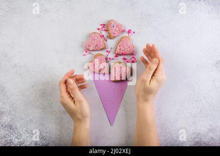 Biscotti rosa in forma di cuore in carta di mais come bouquet di fiori San Valentino giorno o madre giorno concetto fatto in casa. Mani donna Foto Stock