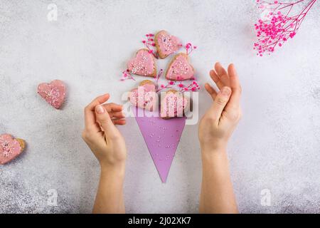 Biscotti rosa in forma di cuore in carta di mais come bouquet di fiori San Valentino giorno o madre giorno concetto fatto in casa. Mani donna Foto Stock