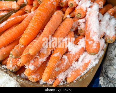 carote, cumuli di carote fresche e mature ricoperte di neve in un mercato aperto o scaffale di negozi di alimentari o scaffale con fuoco selettivo e effcets di rumore Foto Stock