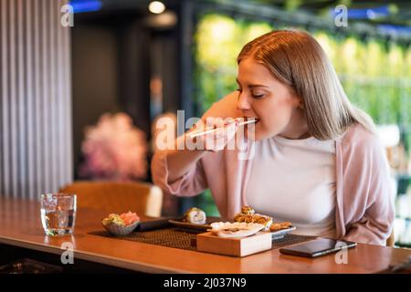 La giovane donna sta mangiando sushi con bacchette al ristorante sushi. Foto Stock