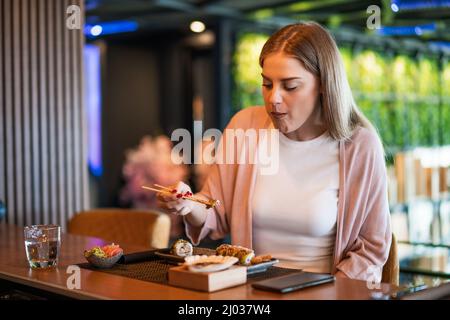 La giovane donna sta mangiando sushi con bacchette al ristorante sushi. Foto Stock