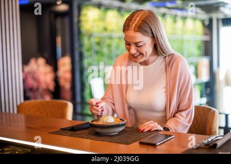 Giovane donna felice sta mangiando il dessert al ristorante. Foto Stock