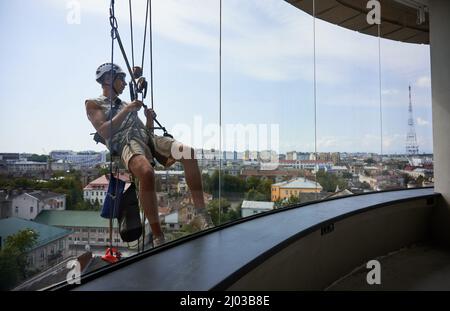 Lavoratore di alpinismo industriale appeso su corda e finestra di pulizia. Vista dall'interno dell'edificio. Pulire utilizzando un'attrezzatura di sollevamento di sicurezza durante la pulizia del vetro di un edificio alto. Foto Stock