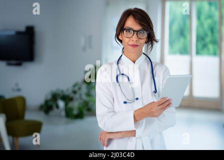 Ritratto di una dottoressa che tiene la cartella paziente su un tablet digitale mentre si trova nel corridoio dell'ospedale. Foto Stock