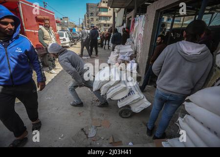 Città di Gaza, territori palestinesi. 16th Mar 2022. I palestinesi raccolgono aiuti alimentari da un centro di distribuzione gestito dall'Agenzia delle Nazioni Unite per il soccorso e l'occupazione (UNRWA). I prezzi dei prodotti alimentari a Gaza City sono saliti dopo l'invasione russa dell'Ucraina. Alcuni rifugiati vendono l'aiuto alimentare, che comprende farina, olio da cucina, riso, lenticchie e latte; per garantire i soldi per la loro vita. Credit: Mohammed Talatene/dpa/Alamy Live News Foto Stock