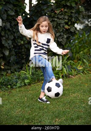 Shes ha ottenuto una certa abilità. Scatto di una bambina che gioca con una palla di calcio in un giardino. Foto Stock