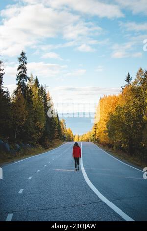 il viaggiatore attivo di brunette in una giacca rossa trova la sua strada attraverso la vita. Un esploratore di 20 anni fa cammina lungo la strada principale attraverso i boschi autunnali. K Foto Stock