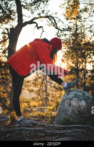 Il viaggiatore attivo bruna lega la sua scarpa sulla cima di una collina su una roccia. Tramonto sulla cima di una montagna a Vuokatti, regione di kainuu, Finlandia. Sorriso naturale Foto Stock