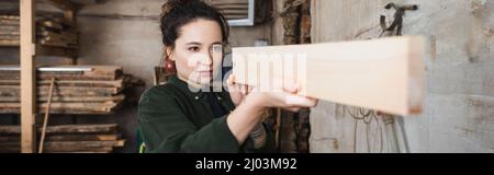 Carpentiere che controlla asse di legno in officina, banner Foto Stock