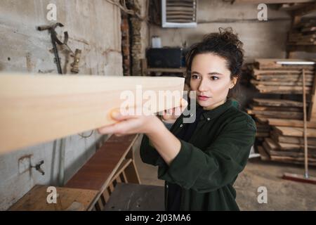 Carpentiere che controlla la tavola di legno sfocata in officina Foto Stock