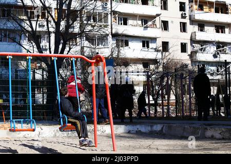 Kiev, Ucraina. 15th Mar 2022. Un bambino siede su un altalena e guarda l'edificio residenziale soffiato da un razzo russo a kiev. Le forze russe continuano la loro invasione su vasta scala in Ucraina. Finora la loro offensiva ha fatto fuggire fino a 2 milioni di persone, attirando critiche e proteste da persone di tutto il mondo. Credit: SOPA Images Limited/Alamy Live News Foto Stock