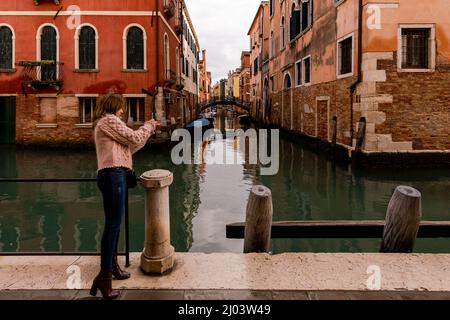 Donna caucasica che fa una foto con il cellulare ai canali di Venezia Foto Stock