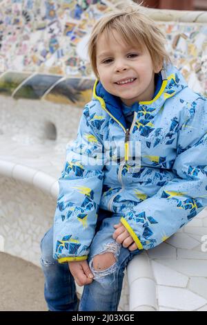 Ragazzino, che mostra il ginocchio ferito da una caduta, seduto su una panchina nel parco Foto Stock