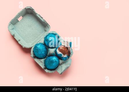 Buona Pasqua. Vista dall'alto delle uova di cioccolato in un cartone blu aperto su sfondo rosa Foto Stock