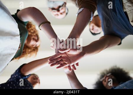 Iniziamo questo progetto. Inquadratura a basso angolo di un gruppo di creativi e allegri uomini d'affari che formano un huddle con le mani all'interno dell'ufficio. Foto Stock