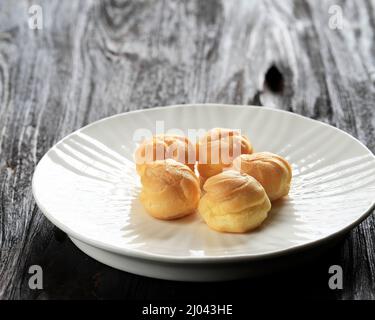 Piccole torte fatte in casa Profiterole Choux Pasticceria con Custard su piastra bianca, tavolo in legno. Isolato Foto Stock