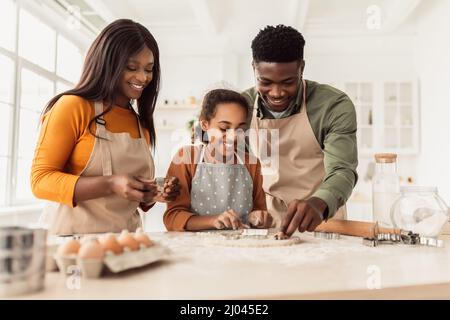 Famiglia nera che fa i biscotti usando le forme di cottura che cucinano in cucina Foto Stock